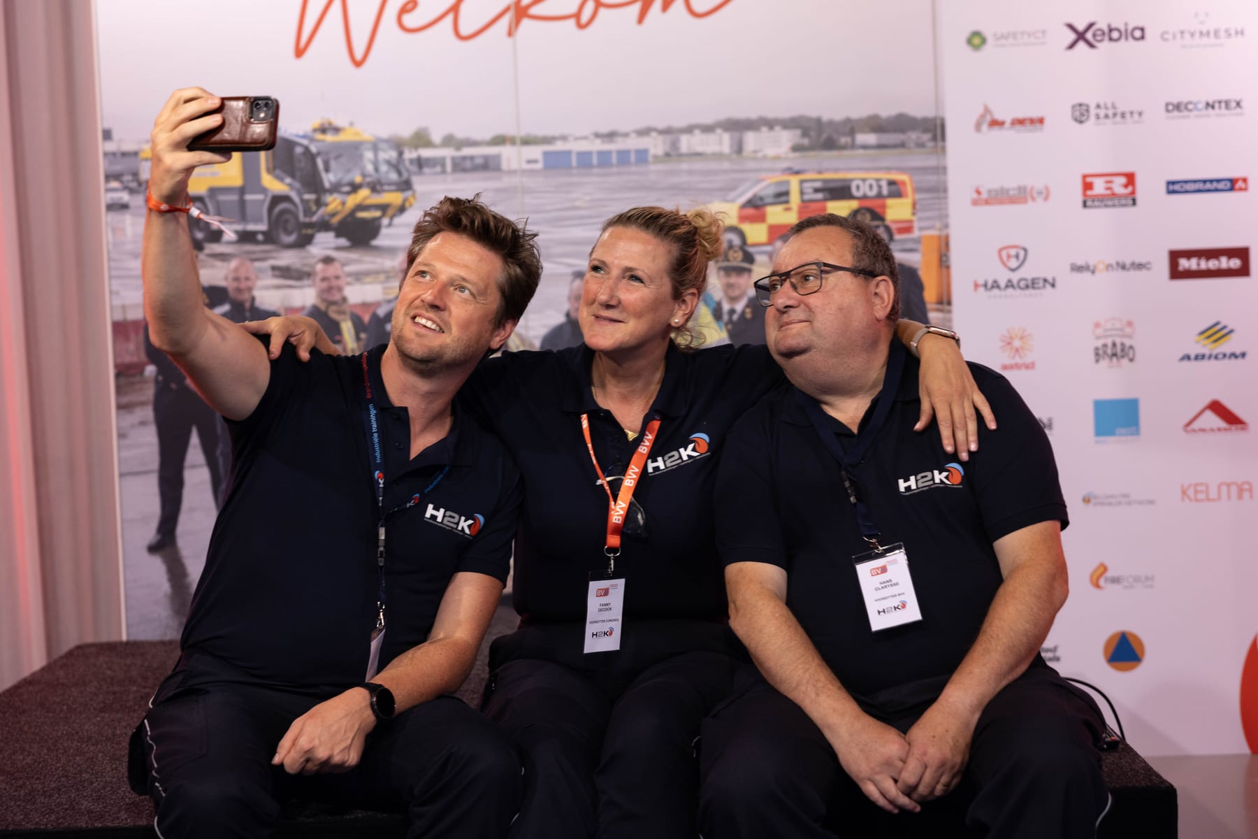 Drie crewleden van het Brandweercongres nemen samen een selfie voor de welkomstwand