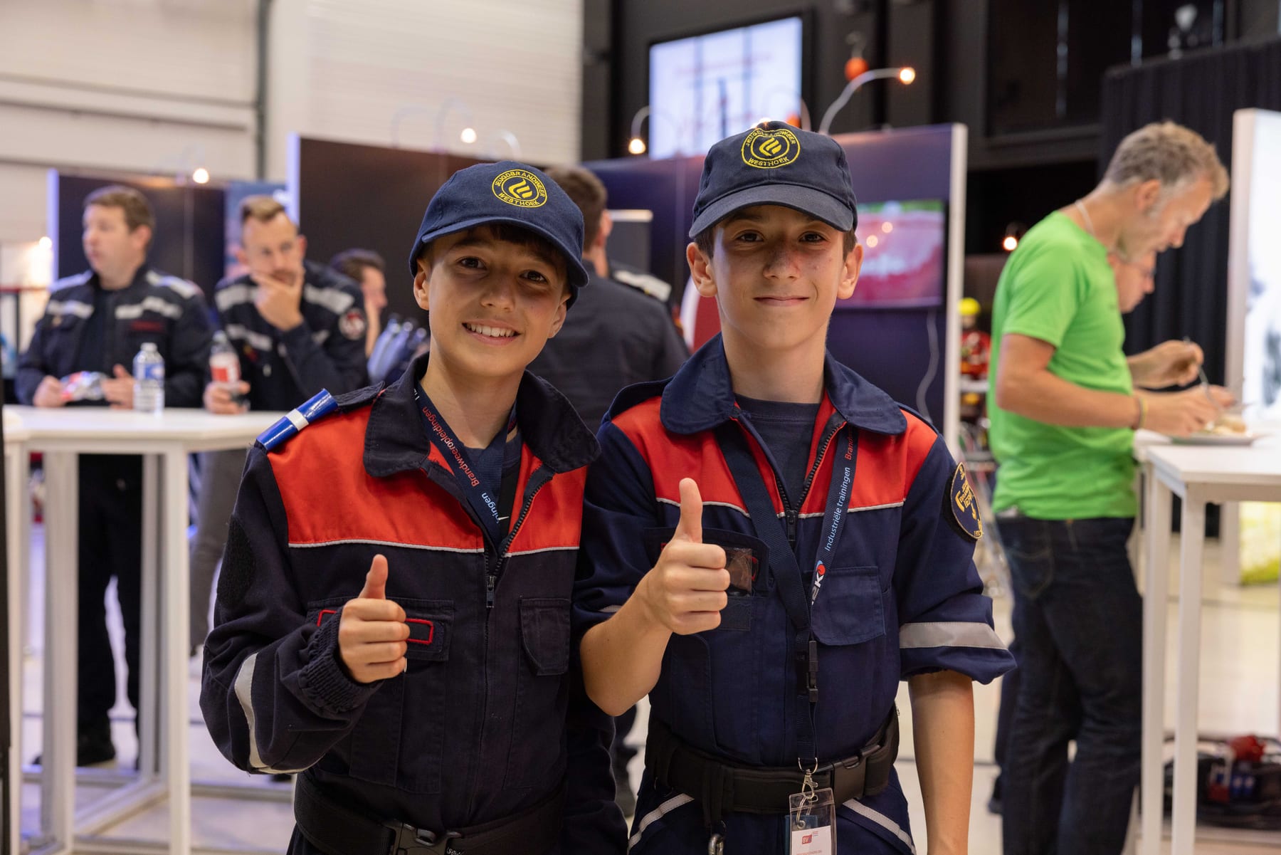 Twee jeugdbrandweerleden steken lachend hun duim op aan een stand op het congres