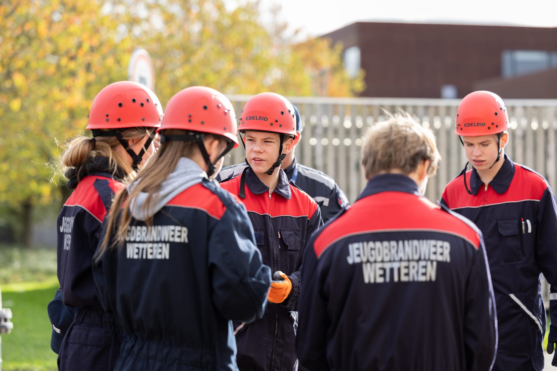 Jeugdbrandweerleden met rode helm overleggen samen buiten tijdens een oefendag
