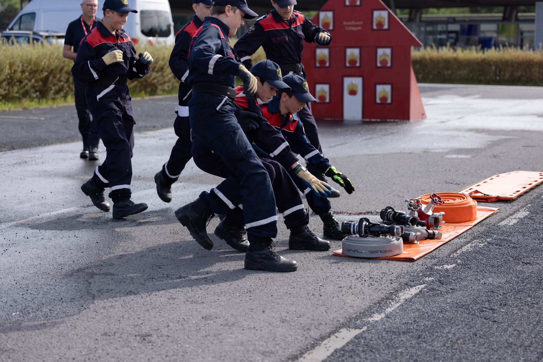 Een ploeg jeugdbrandweerleden loopt met slangen naar een oefenopstelling
