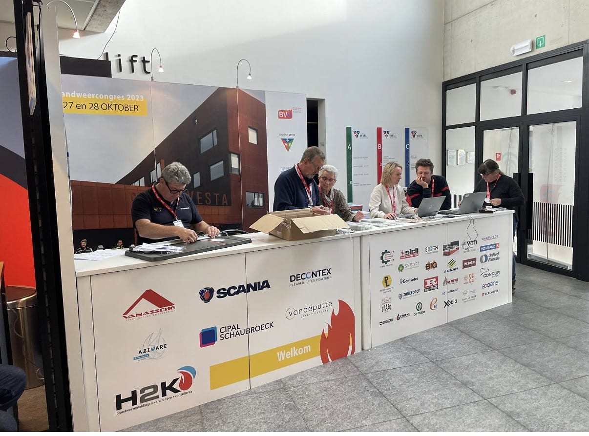 De onthaal- en inschrijfbalie van het Brandweercongres met medewerkers en partnerlogo's